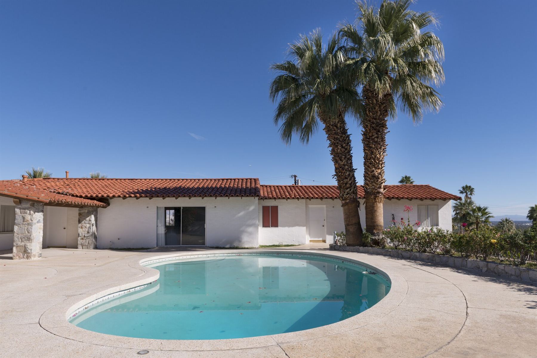 White home with a red tile roof, palm trees, and a pool