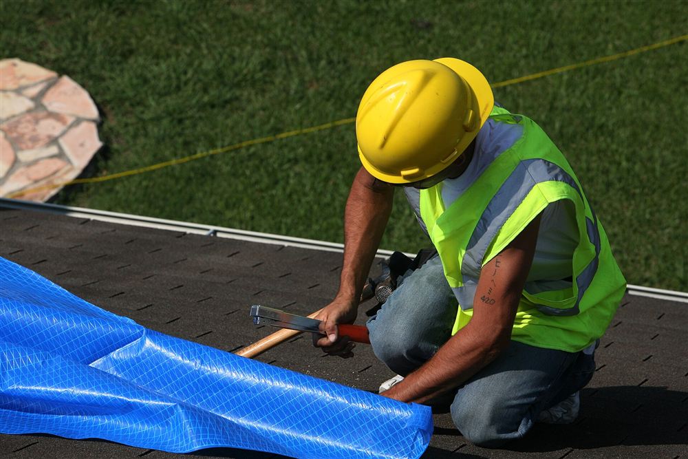 Roofer in a hard hat hammering on a roof